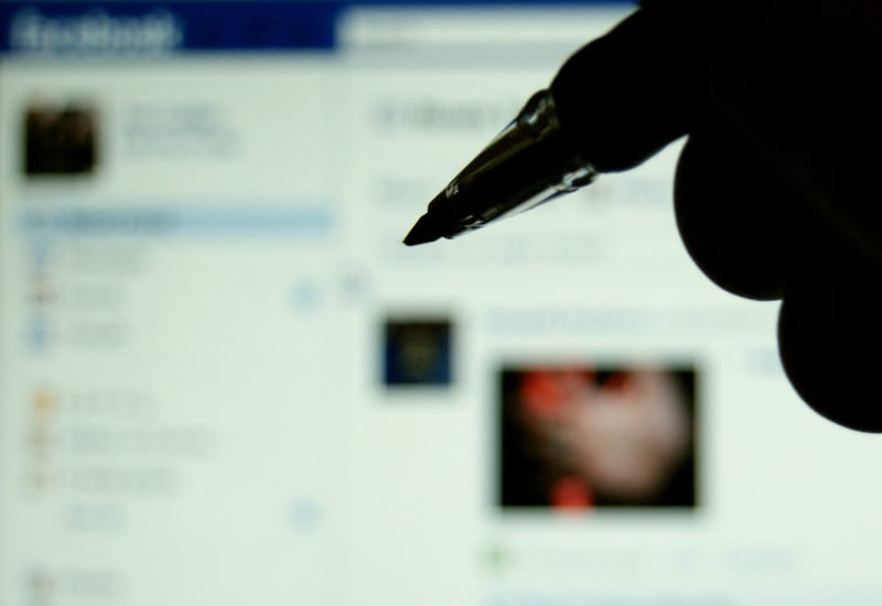 hand holding a pen, a computer screen displays Facebook in the background