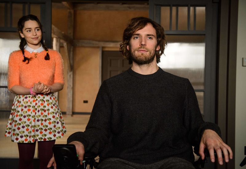 Screen capture of main character in a wheelchair looking forwards pensively in the foreground, main female lead in the background looking at him and smiling, clasping her hands.