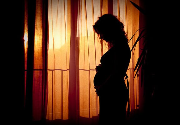 A pregnant woman gazing at her belly in front of a window